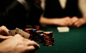 stół pokerowy z żetonami i kartami, otoczony przez kilka osób