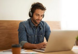 młody mężczyzna ze słuchawkami na uszach pisze na laptopie