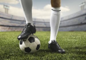 zawodnik przytrzymujący stopą piłkę na boisku futbolowym
