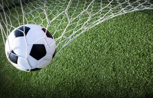 piłka wpadająca do bramki na tle murawy boiska futbolowego