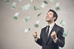 Męzczyzna w garniturze na szarym tle, na którego z góry lecą pieniądze