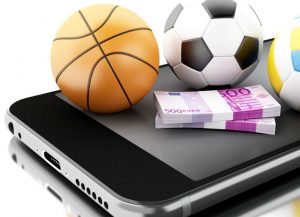 Piłki i plik pieniędzy na telefonie przy tekście o polskim rynku bukmacherskim